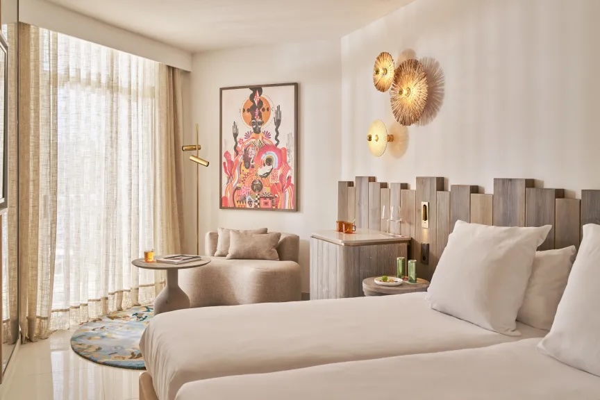 Twin beds with white bedding and art work hanging above and besides it and a little seating area next to the bed