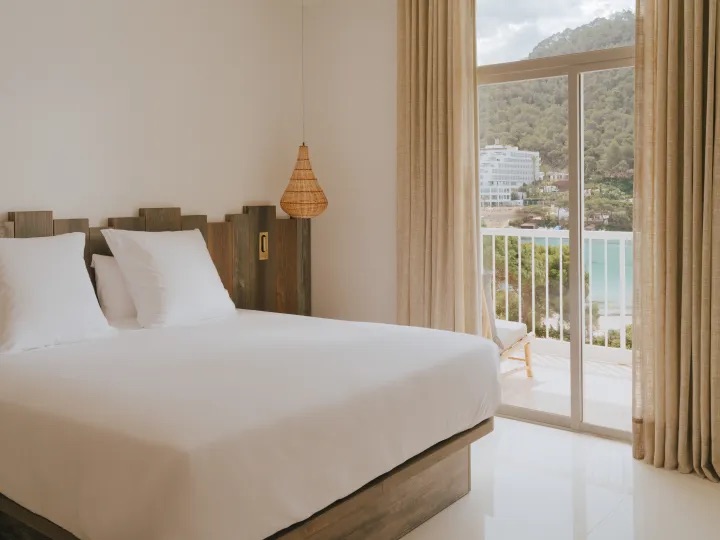 big king sized bed with white bedding and a large window next to it to access the balcony