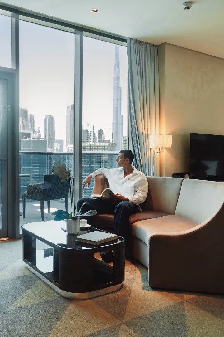 man on a couch looking out the window with the view of dubai