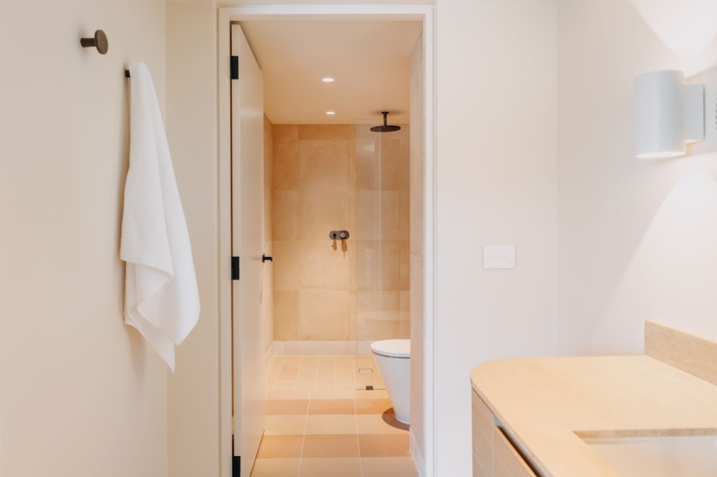 Warm-toned bathroom with a door leading into a rainfall shower.