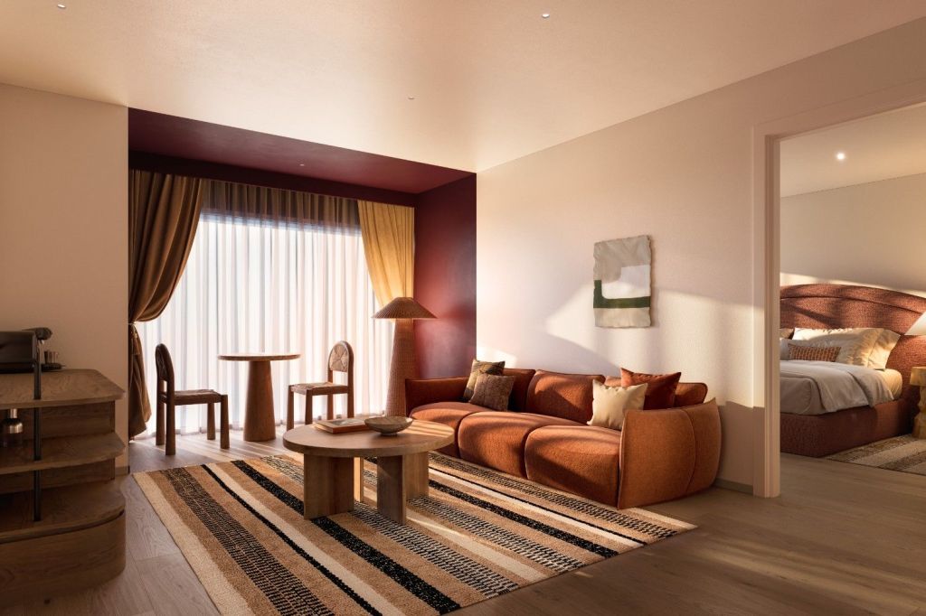 Sunlit hotel suite lounge area with a rust-colored modular sofa, round coffee table, striped rug, and a small dining table.
