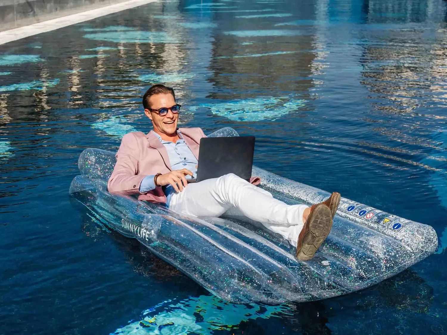 man on floating bed in the pool with a laptop on his lap