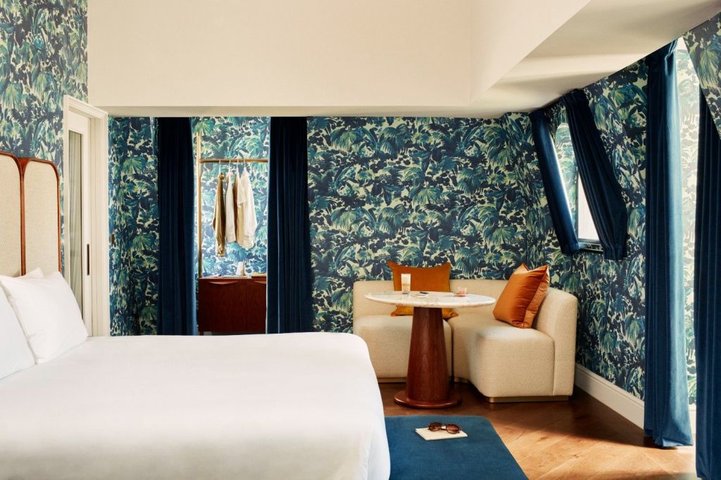 Blue wallpapered suite with beige corner sofa, dark orange cushions, and a white double bed in the room