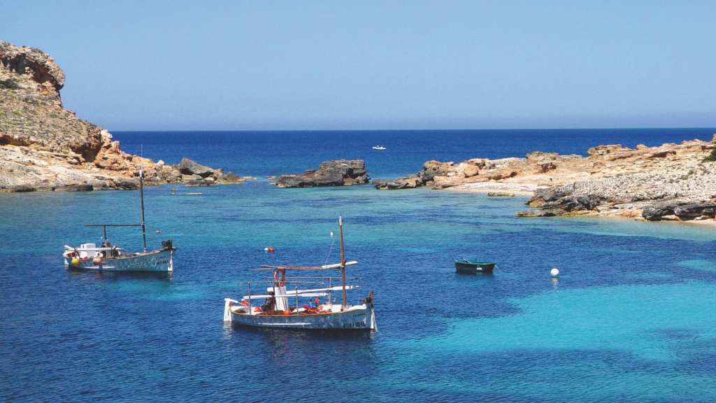 image of couple of little boats in the sea with some rocks on the side