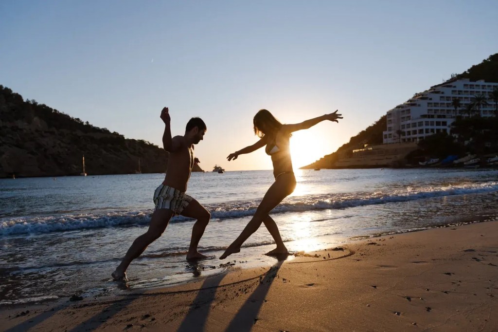Two people playing or running on the beach at sundown