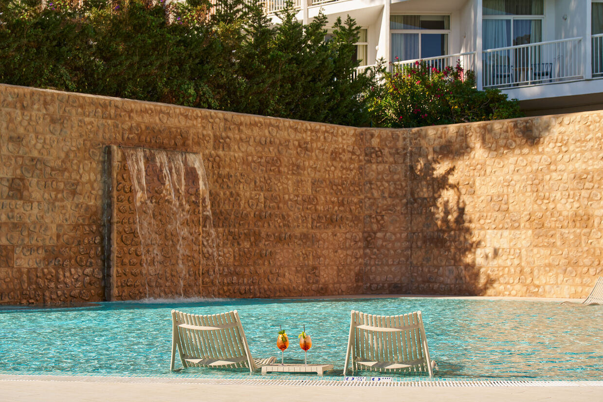 Two subeds in the water of a pool with an orange wall in front of it.
