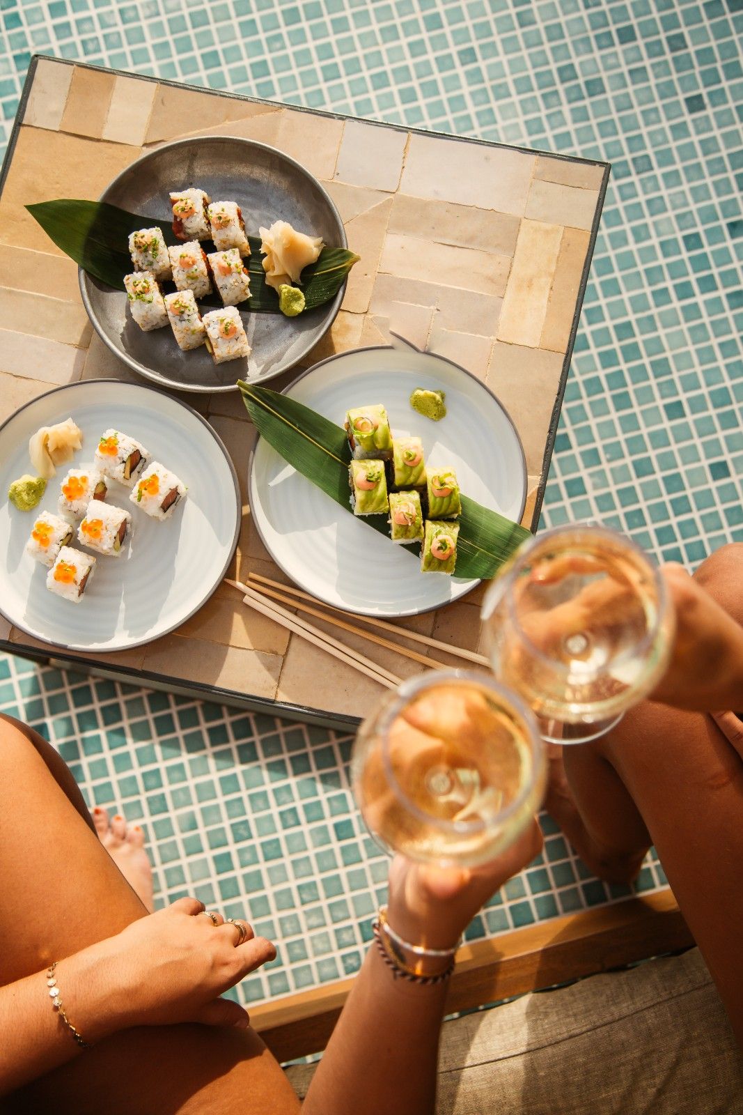 multiple sushi dishes with 2 people holding their drink and cheersing