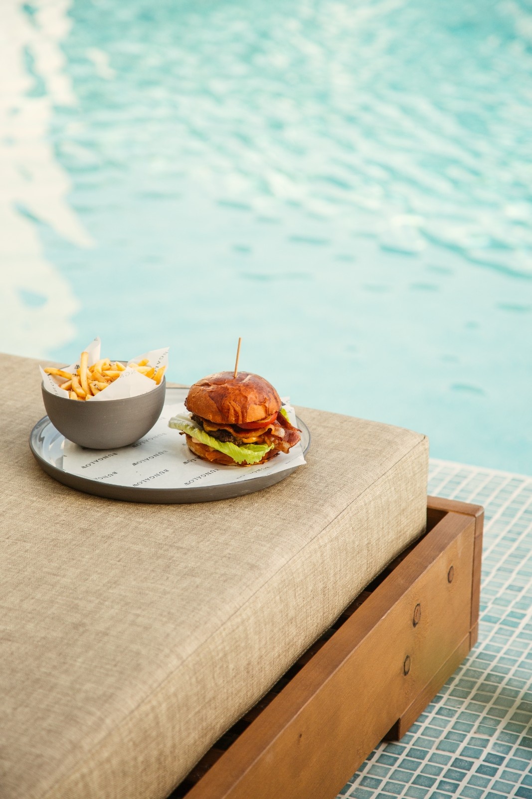 a burger and fries on a plate on a sunbed by the pool