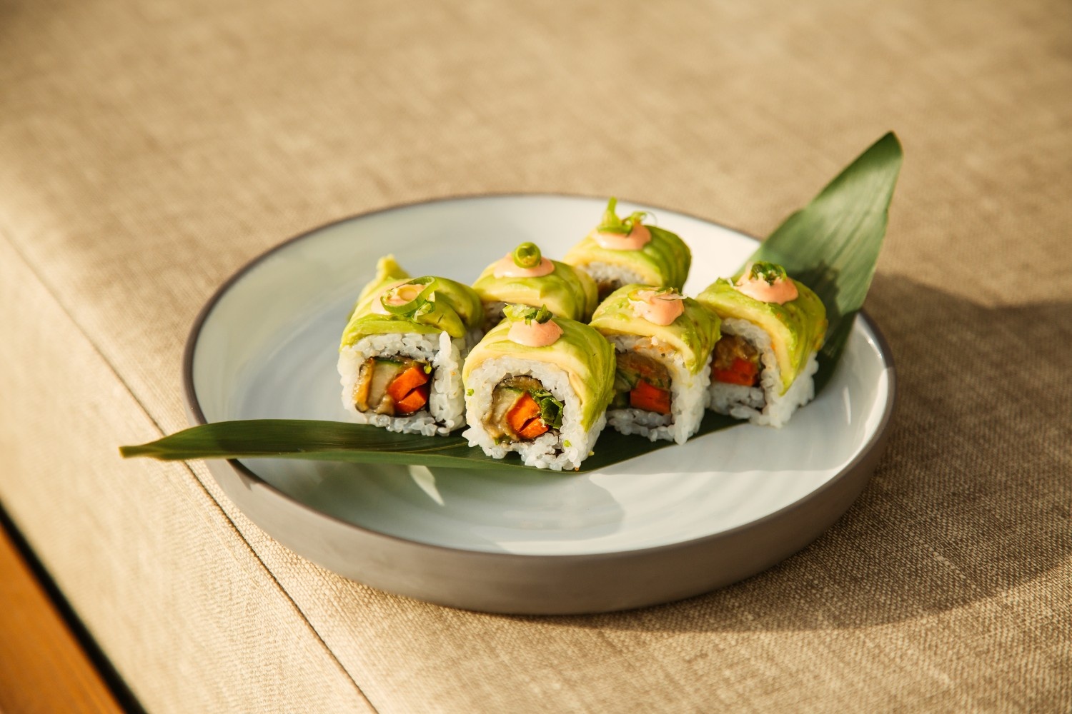 6 pieces of sushi with avocado on top on a plate with a big leave under it