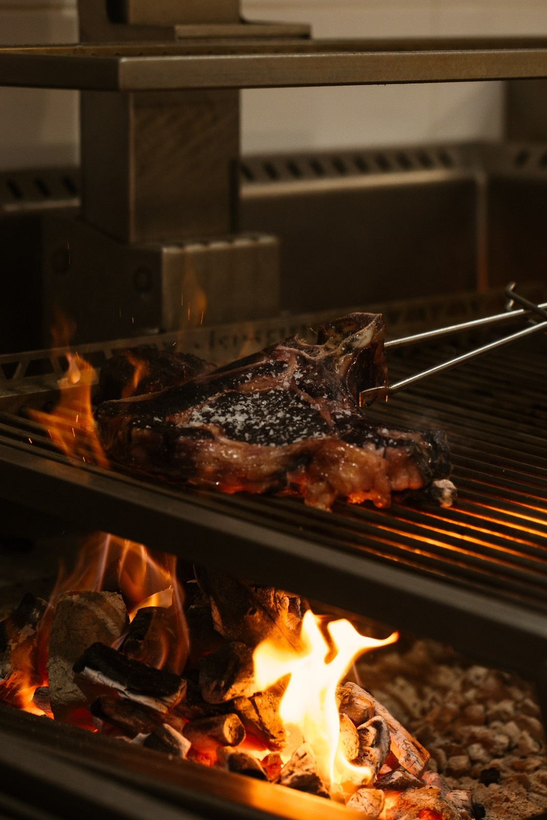 a dark grill with a large piece of meat on it and a big fire under it