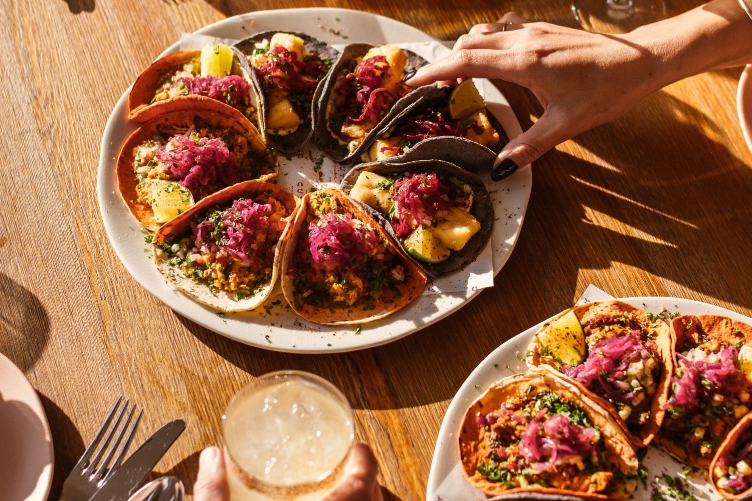 Varios tacos de colores en un plato, con la mano de alguien asomando mientras coge un taco.