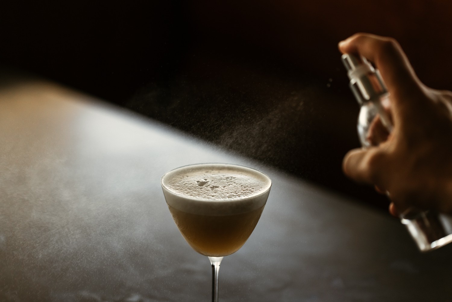 cocktail on a dark table with someone spraying something around it