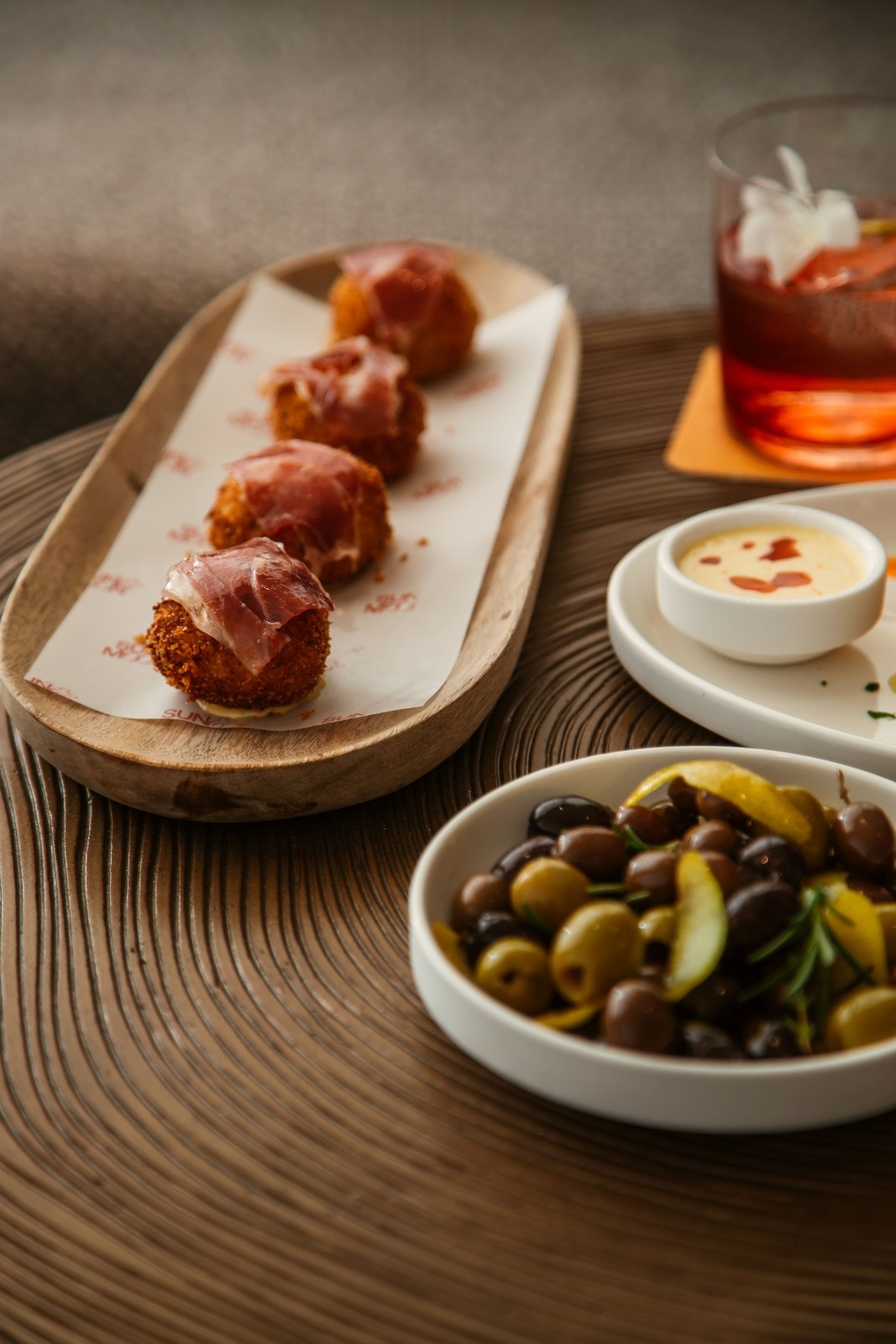 multiple small bites on a table including olives and a drink in the background