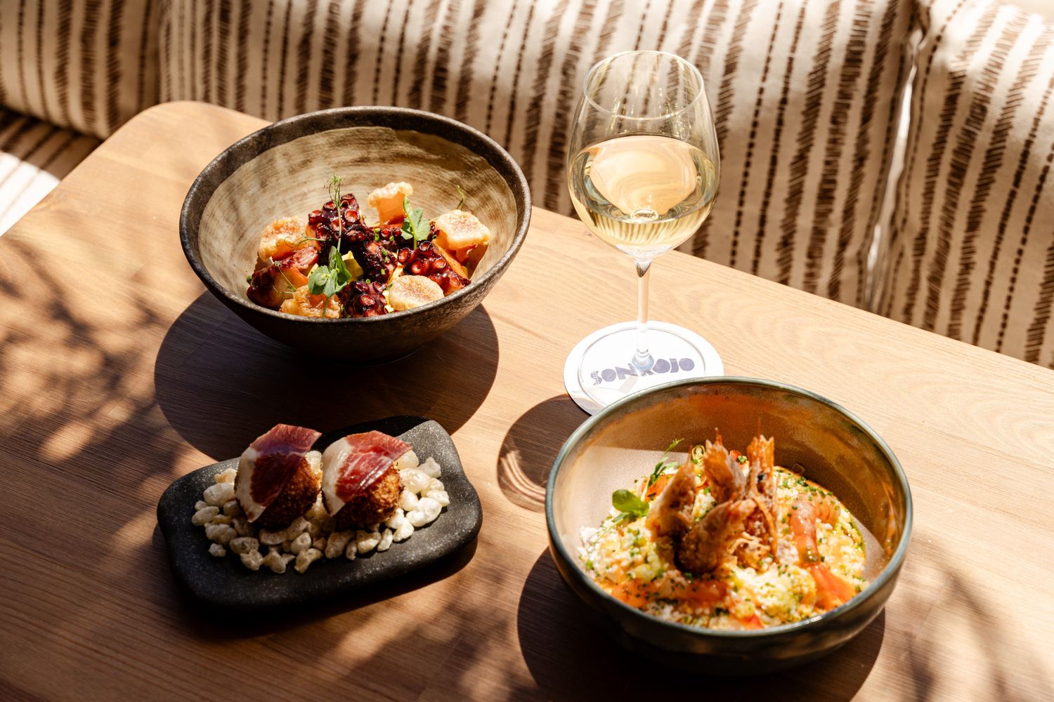 3 plates with food on a table with a full glass of wine next to it