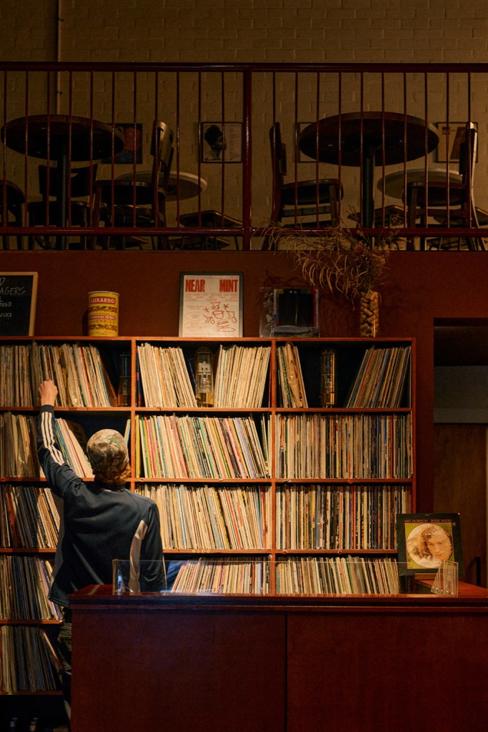 Person near a wall of vinyl records in a warmly lit bar