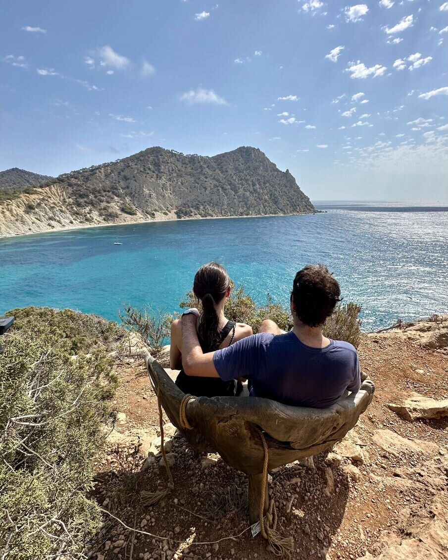 couple sitting on a bench at the top of a hill with the sea as their view