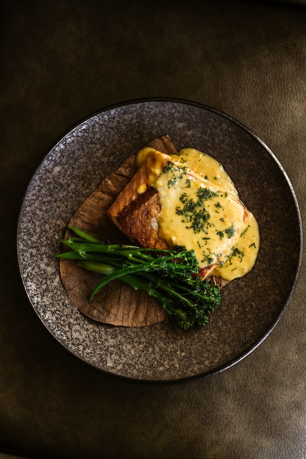 Niko dish on a dark plate, showing a fish dish with a yellow sauce and some broccoli