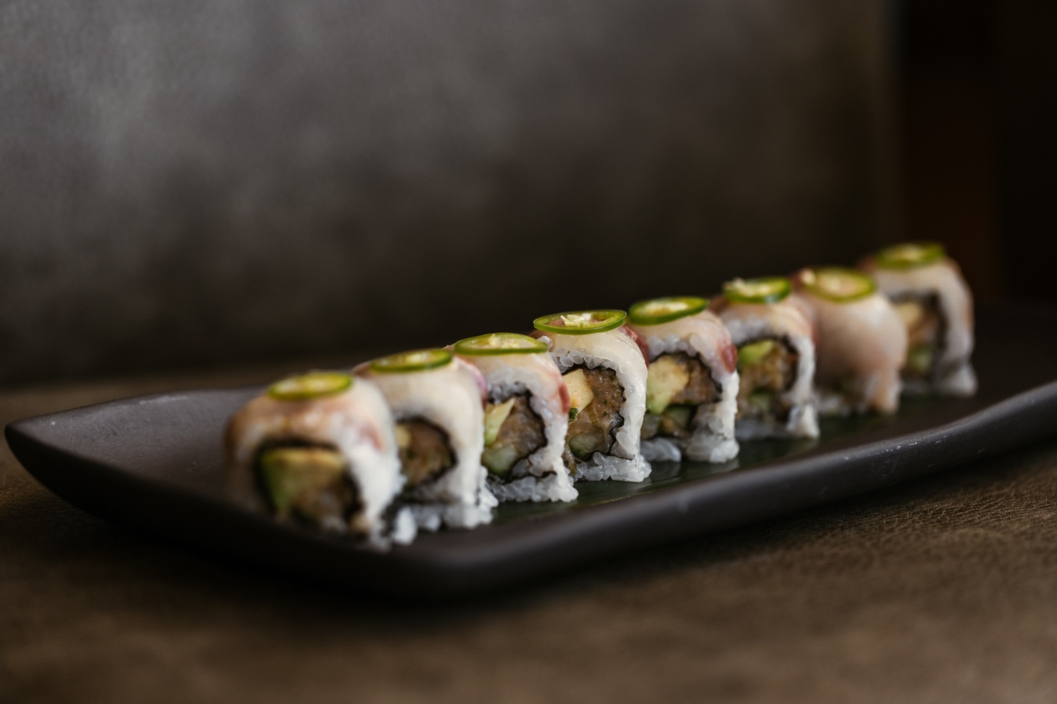 plate of multiple sushis with a green vegetable on top of them
