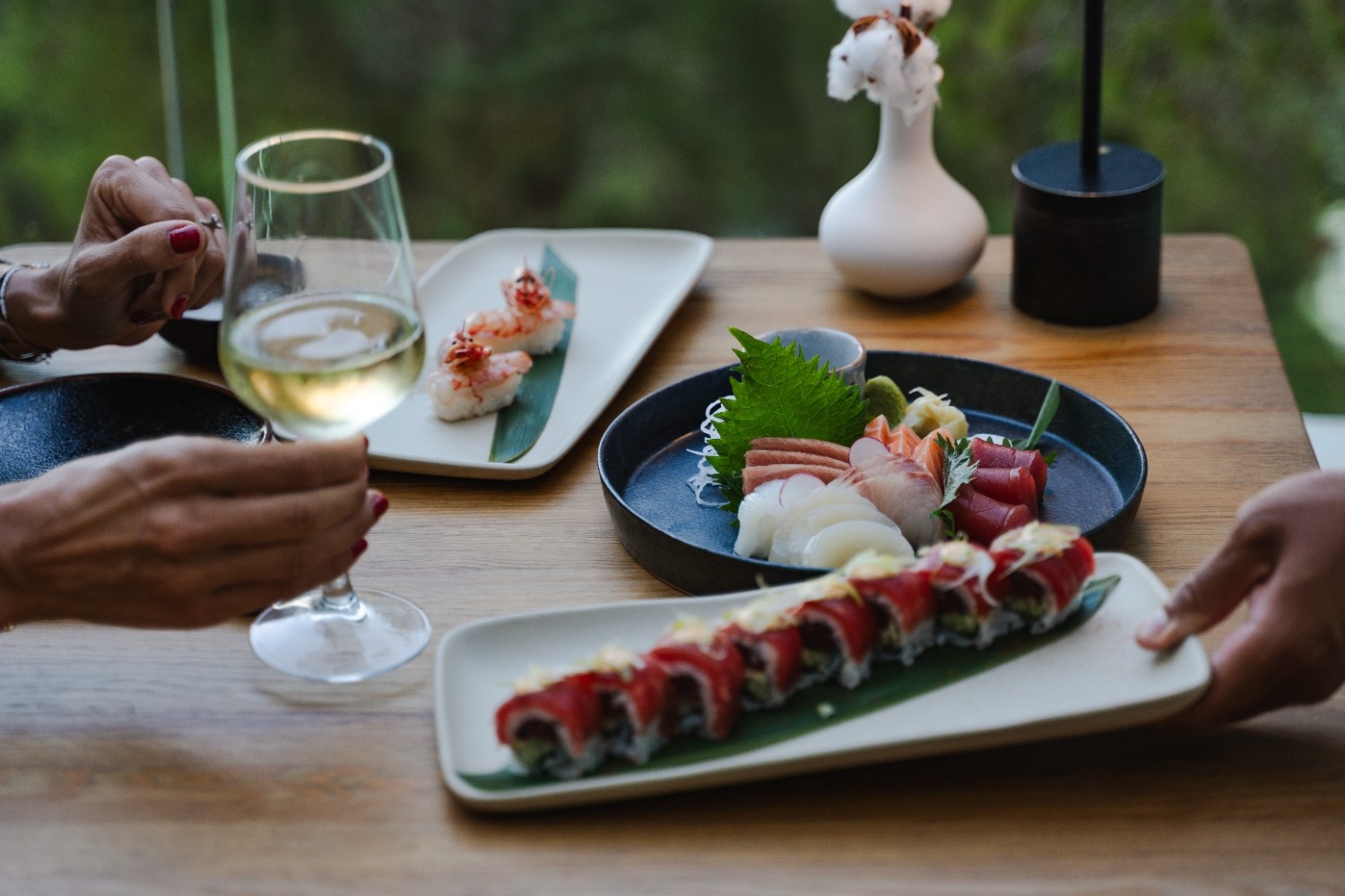 different japanese dishes on a table with hands showing on the side