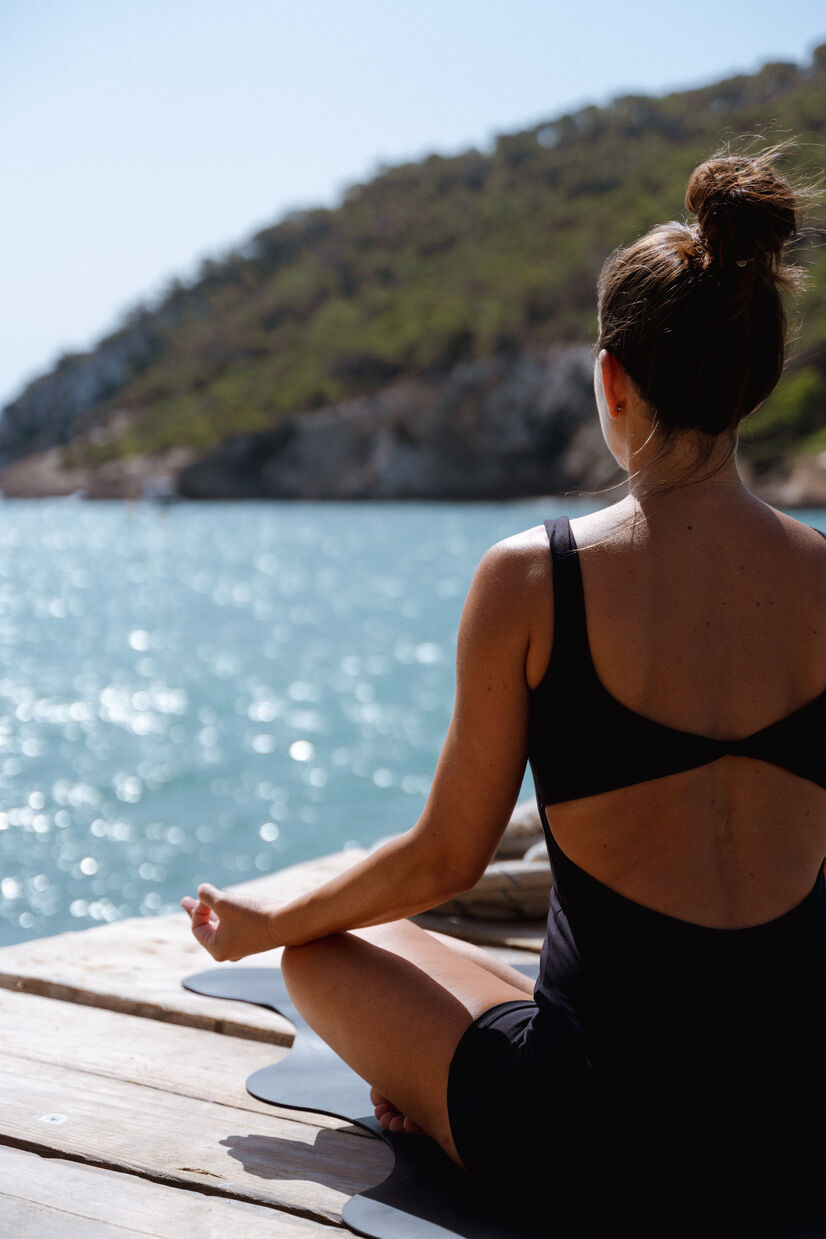 Woman sitting on a deck in front of water practicing yoga