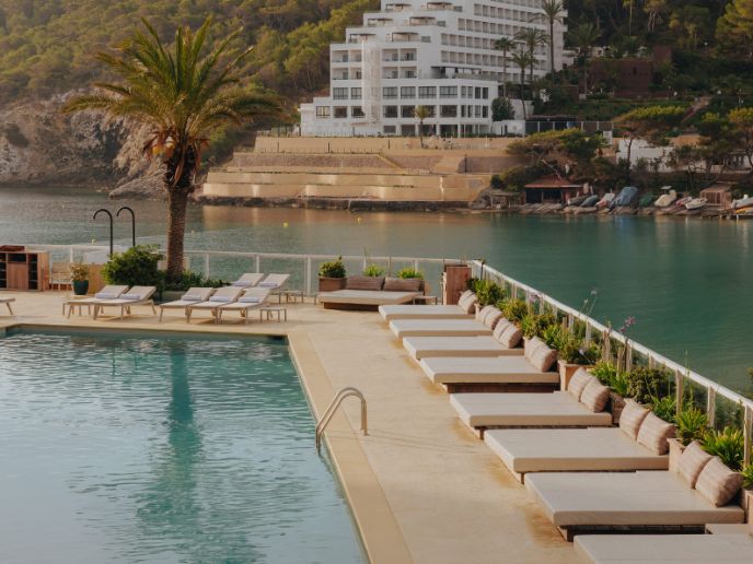 Pool surrounded by sunbeds with the sea and building in the background