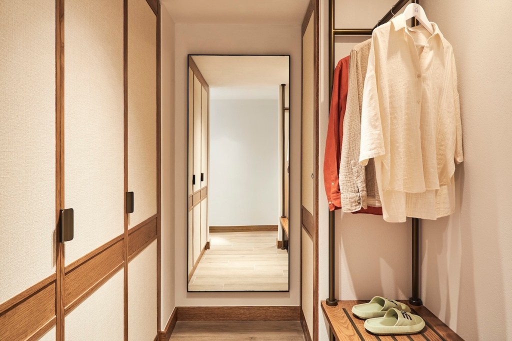 Hallway view of a wardrobe with clothes hanging and a full-length mirror