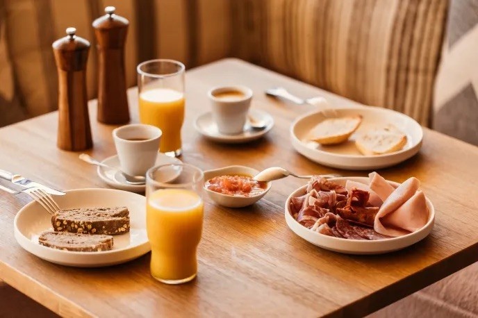 table with multiple breakfast options including an orange juice, some bacon and coffee