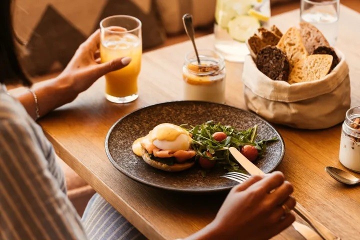 table with multiple breakfast options including an glass of orange juice and eggs with bread
