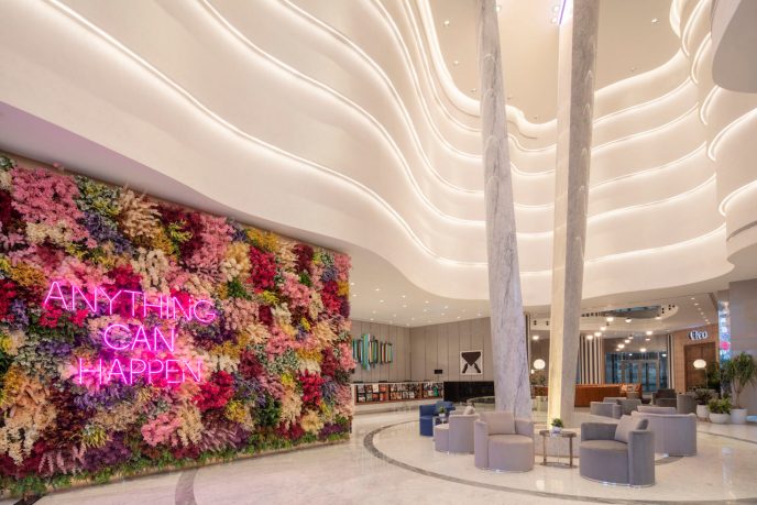 White hotel lobby with colorful flower wall and neon pink sign that says anything can happen