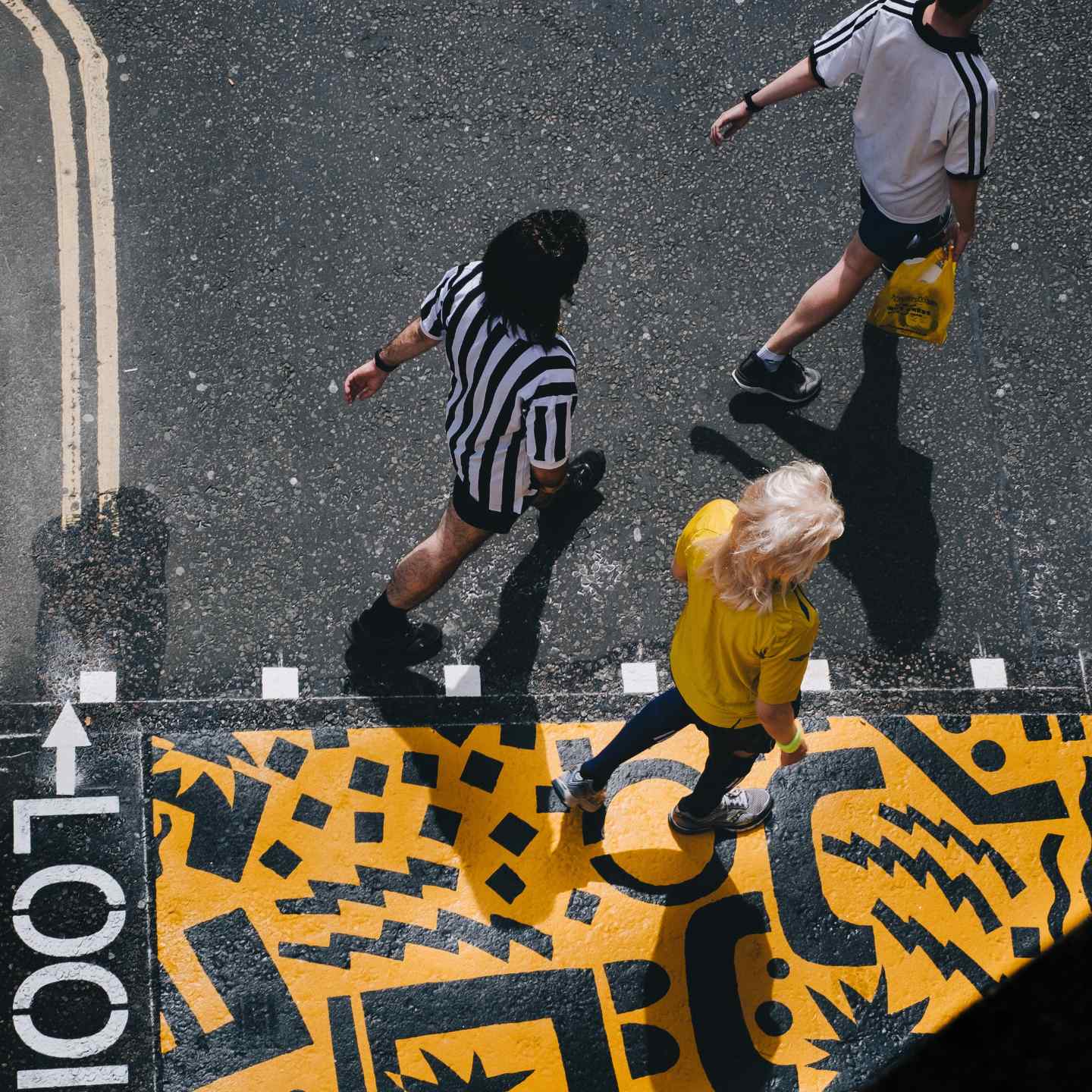 Three friends walking down the street in black and white clothes with yellow and black street art on the ground