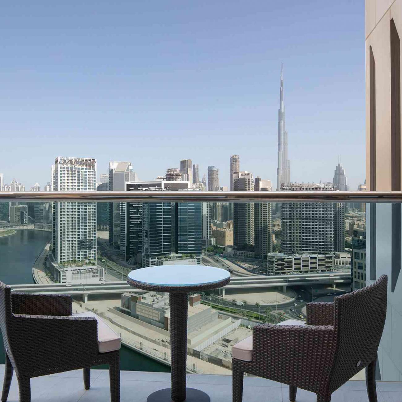 A view from the room balcony with 2 chairs and a coffee table, with a high rise view of Dubai City and Burj Khalifa building