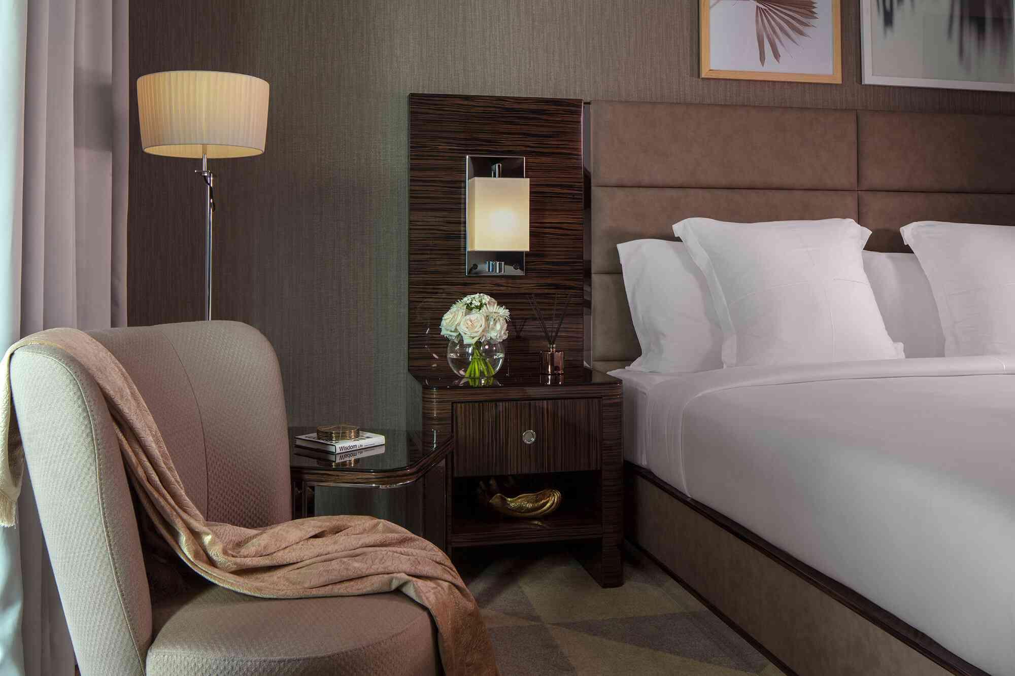 Hyde Dubai General Admission King Room showing a king size bed with bedside tables, cosy armchair with a throw and a floor lamp