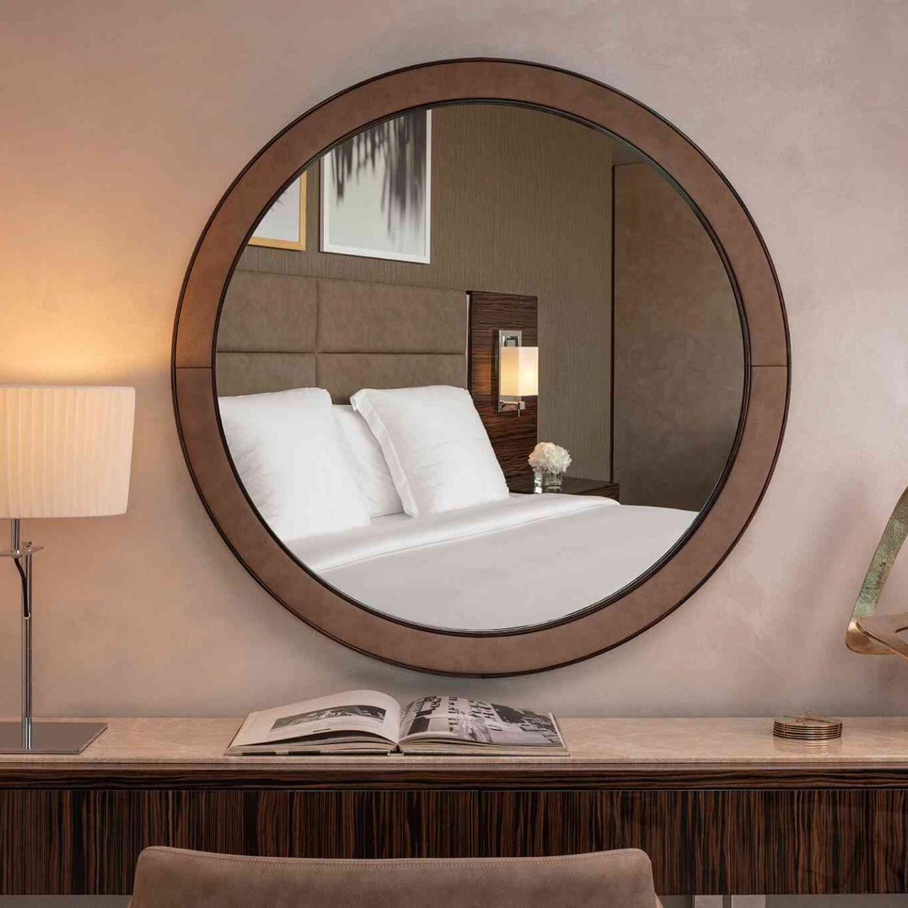 A vanity table with a lap, and round wall mirror that reflects a double bed