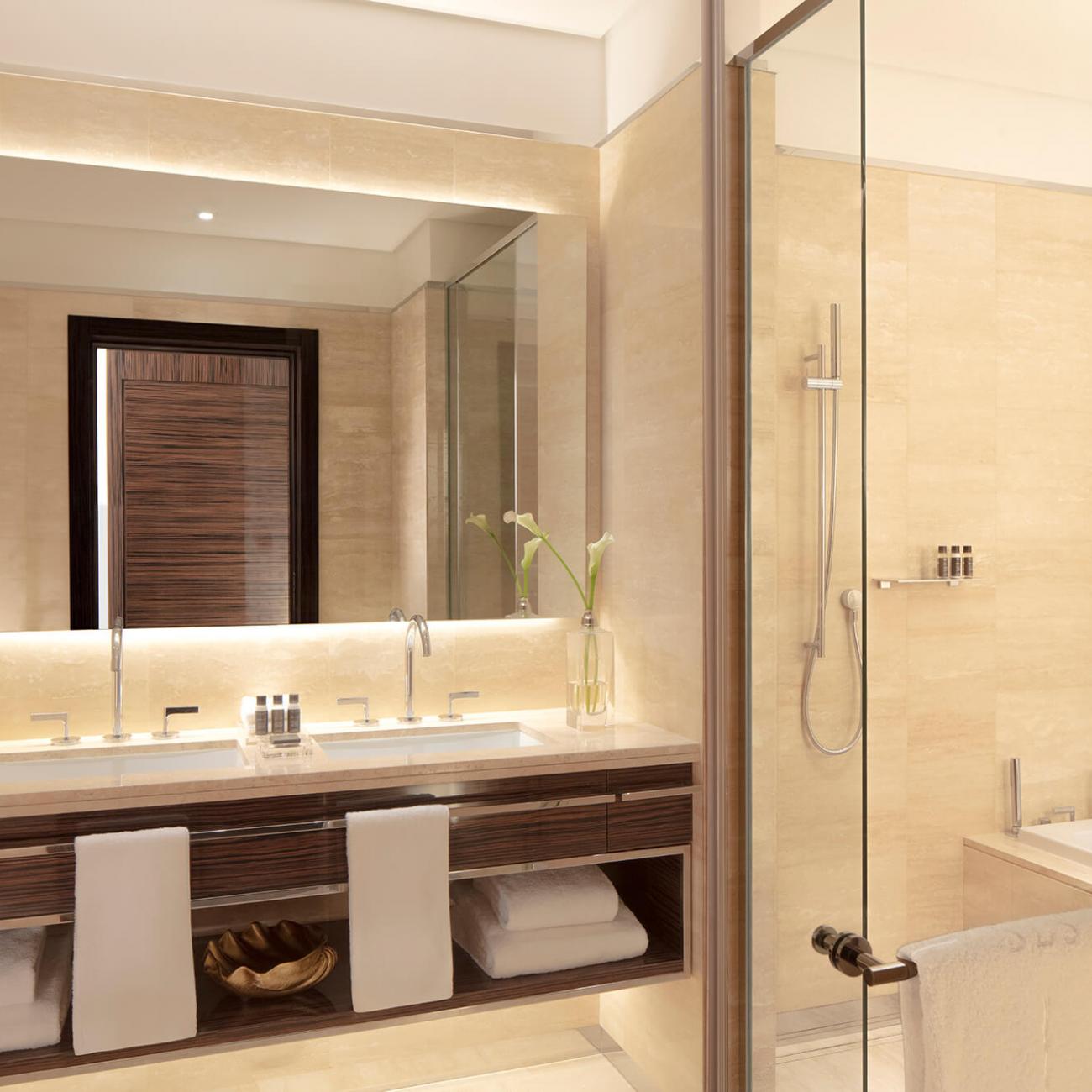 A large bathroom with 2 sinks on the background, with a walk in section with shower and bathtub on the right
