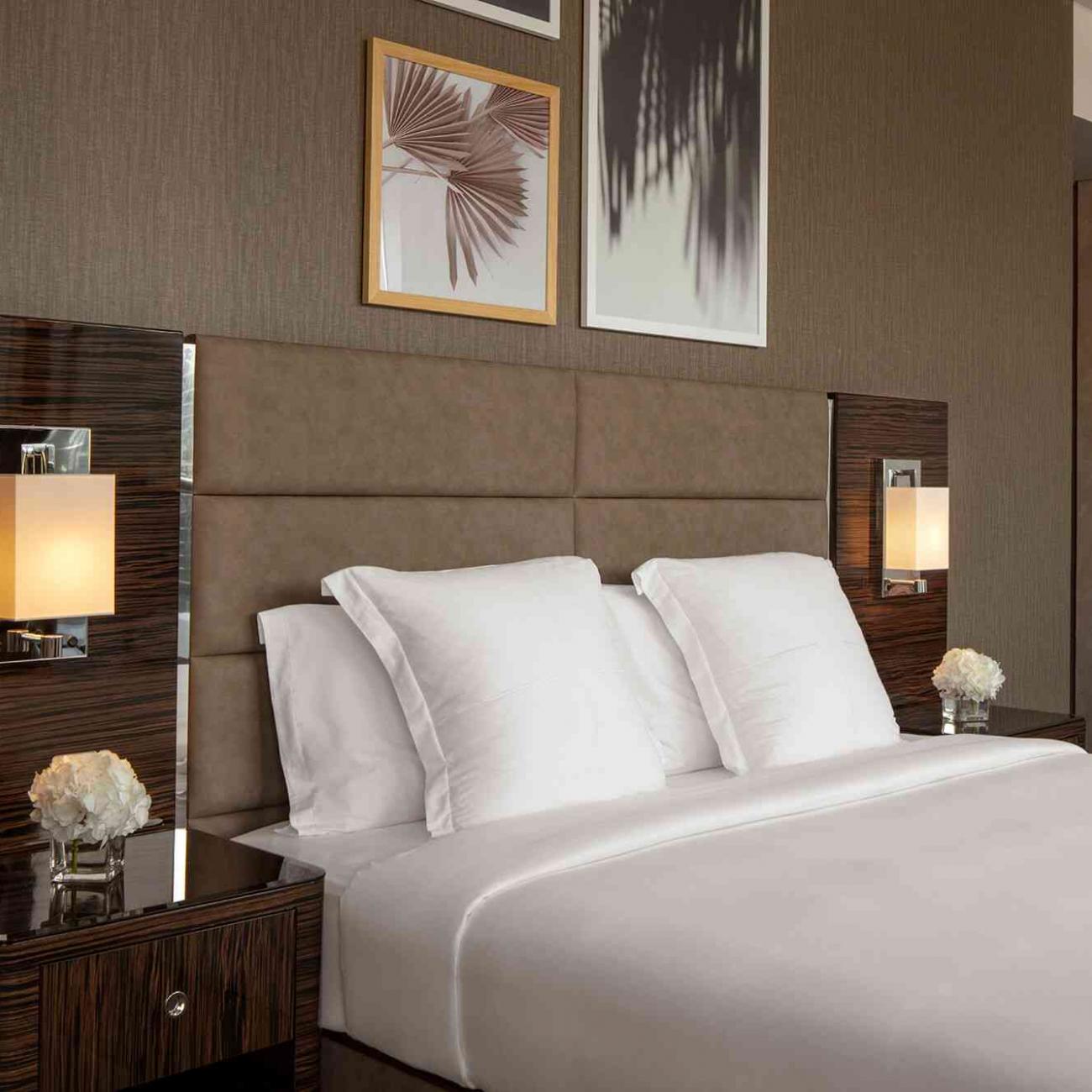 A king size bed with bedside tables and lamps, with several art prints on the wall