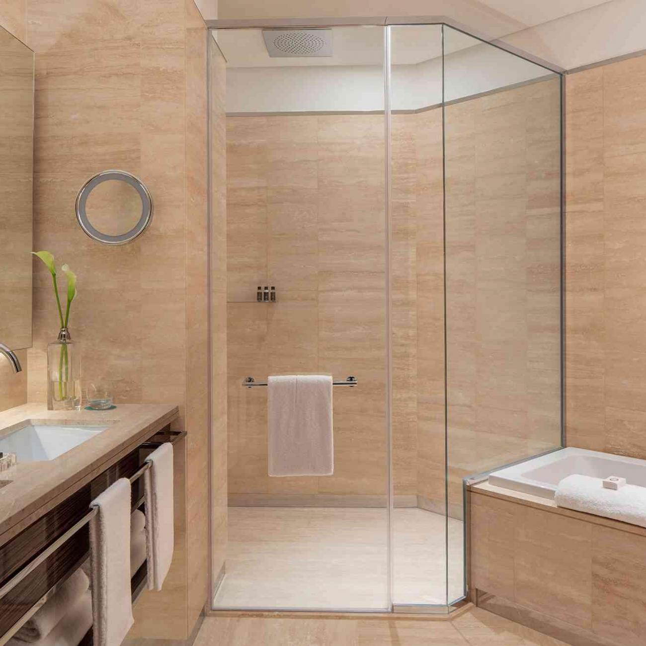 Large bathroom with 2 sinks on the left, walk in glassed shower at the centre, and a bathtub to the right.