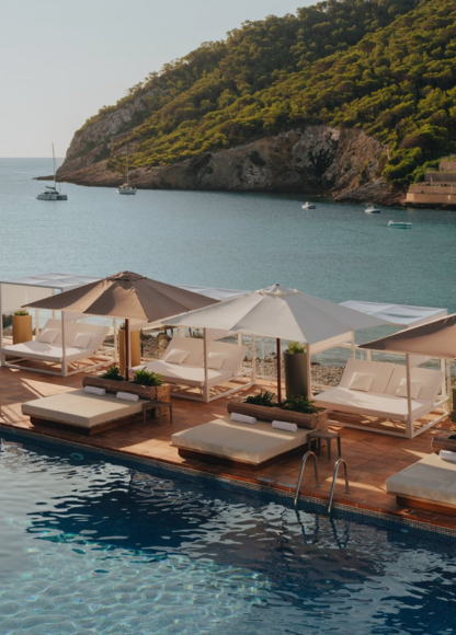 Cabañas sobre grandes tumbonas acolchadas con piscina a un lado y mar y montañas al otro en Hyde Ibiza.