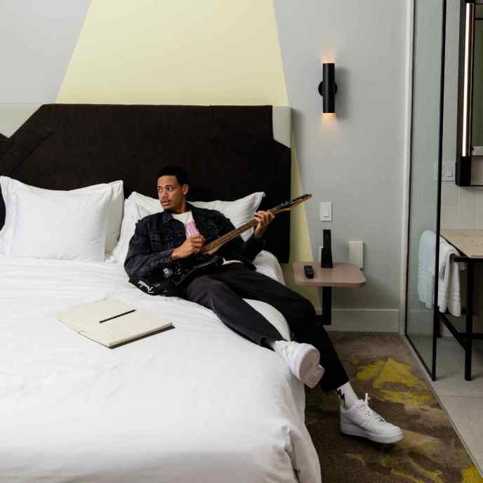 Man laying on white bed holding a black guitar