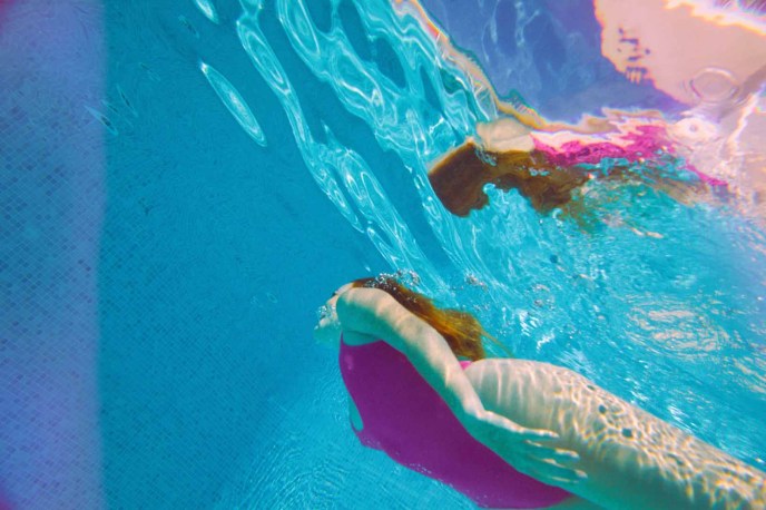 Girl in pink bathing suit swimming in pool underwater