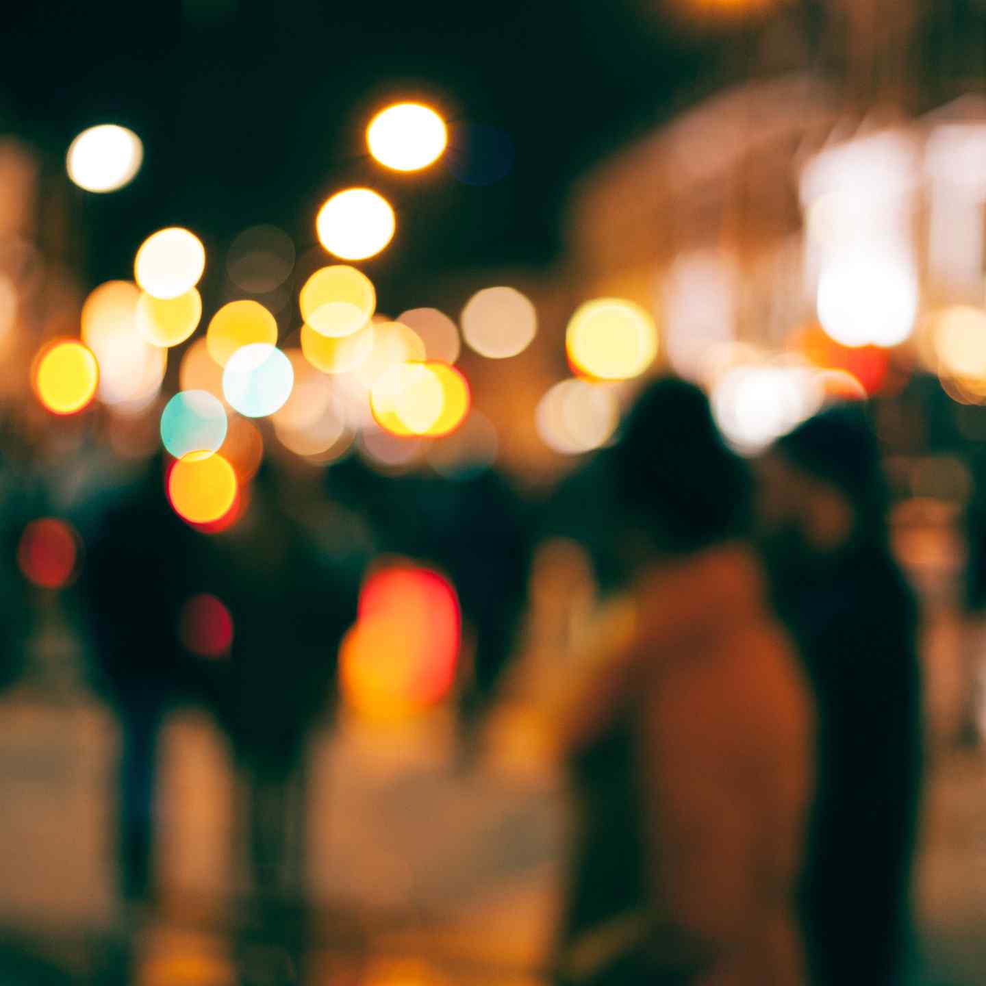 Blurry cityscape of people walking at night with headlights in the background