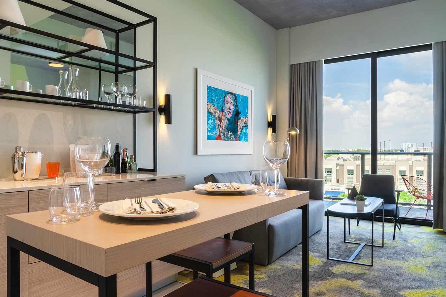 Kitchen dining area for a hotel suite, with sofa in the background, balcony view of the city