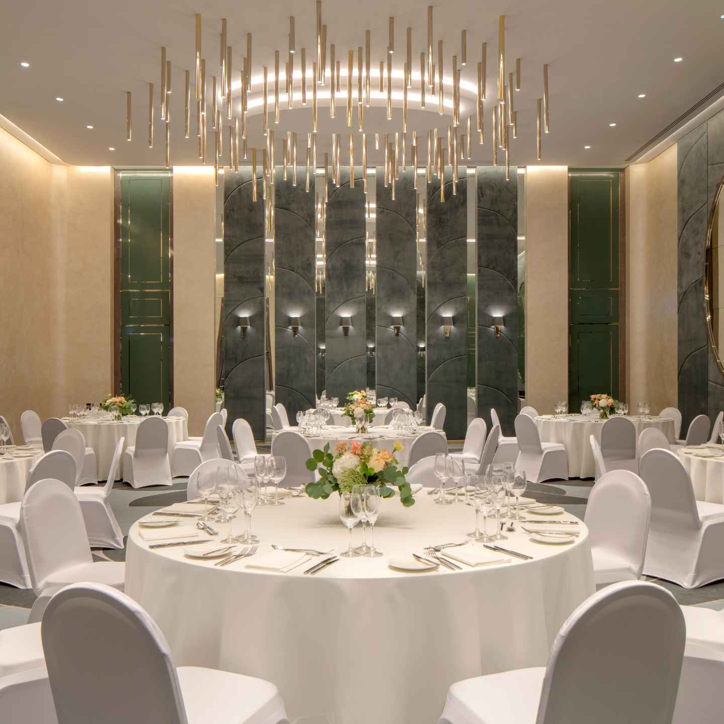 White round tables with white covered chairs in brightly lit ballroom with golden chandelier