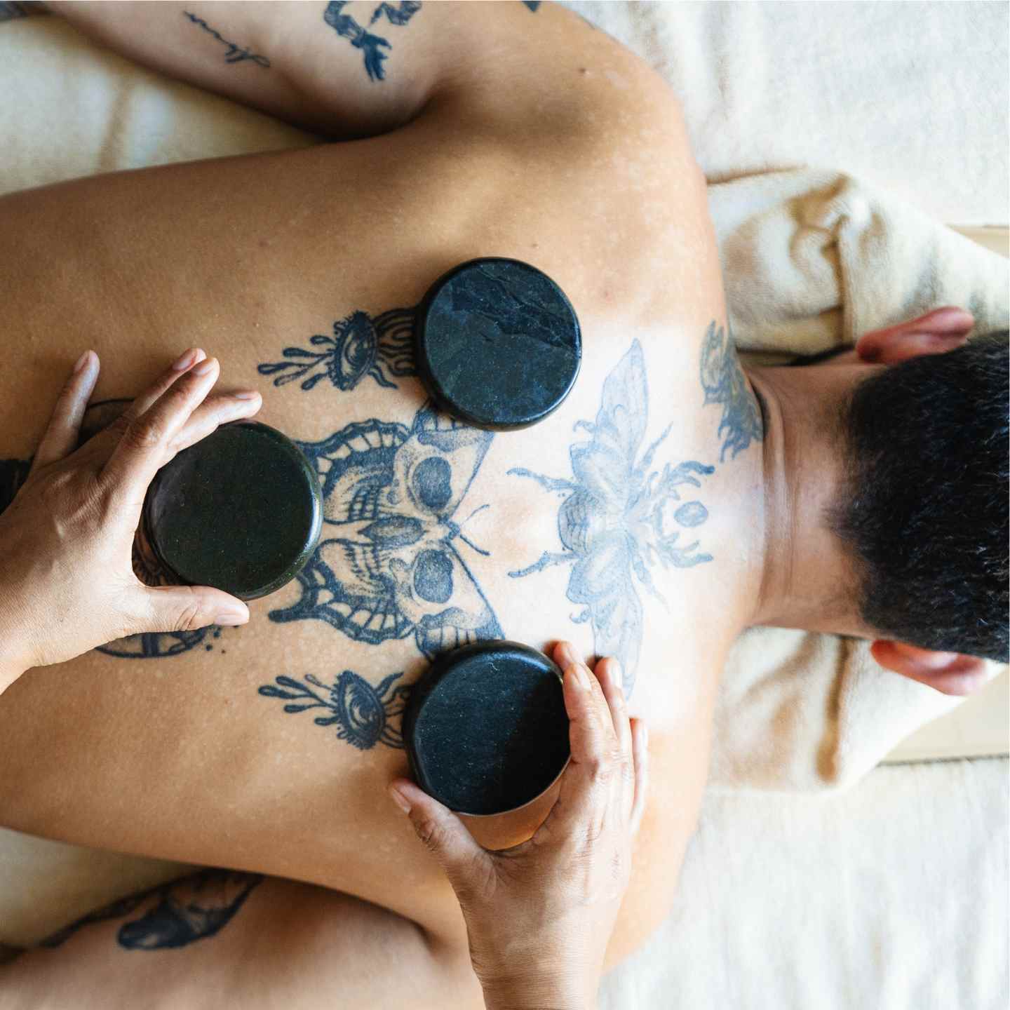 Man with tattoos on back laying on spa bed with black stones on his back