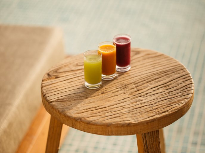 Green, orange, and red juices in glass cups sitting on a wooden stool