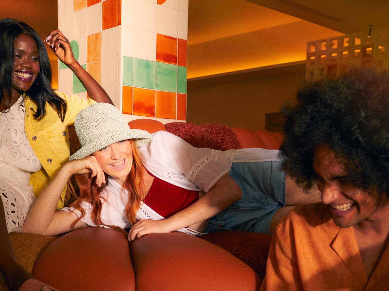 Una chica sentada en un sofá de cuero, otra chica tumbada en un sofá y un amigo sentado debajo de ellas en el vestíbulo de Hyde Ibiza.