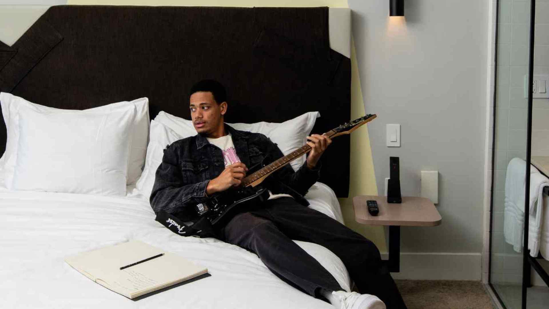 Man lying on white bed holding a black guitar