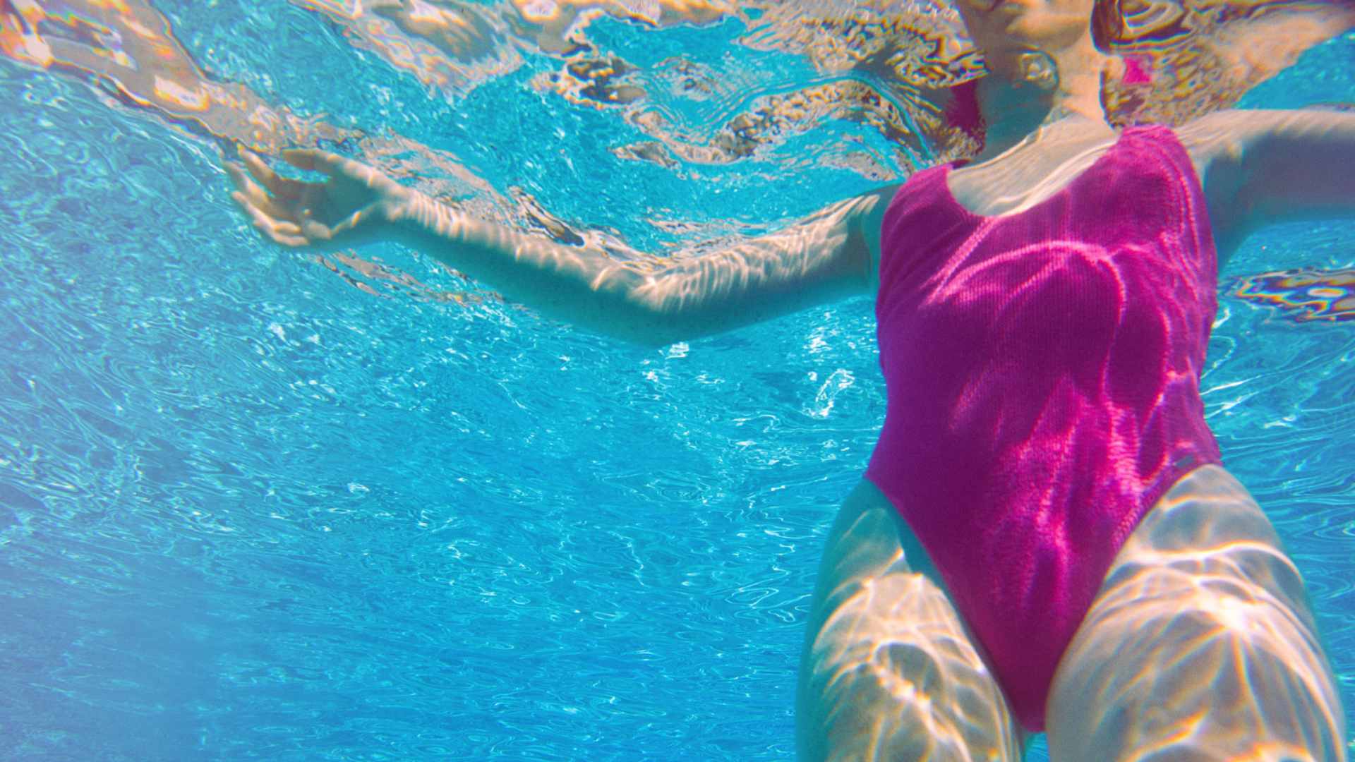 Woman in pink bathing suit underwater in a blue pool