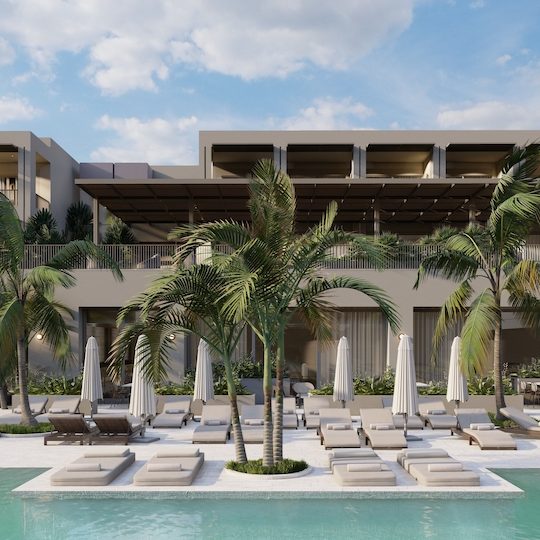 Large pool deck area with rows of chaise lounges and umbrellas with palm trees and beige building in the background with multiple stories