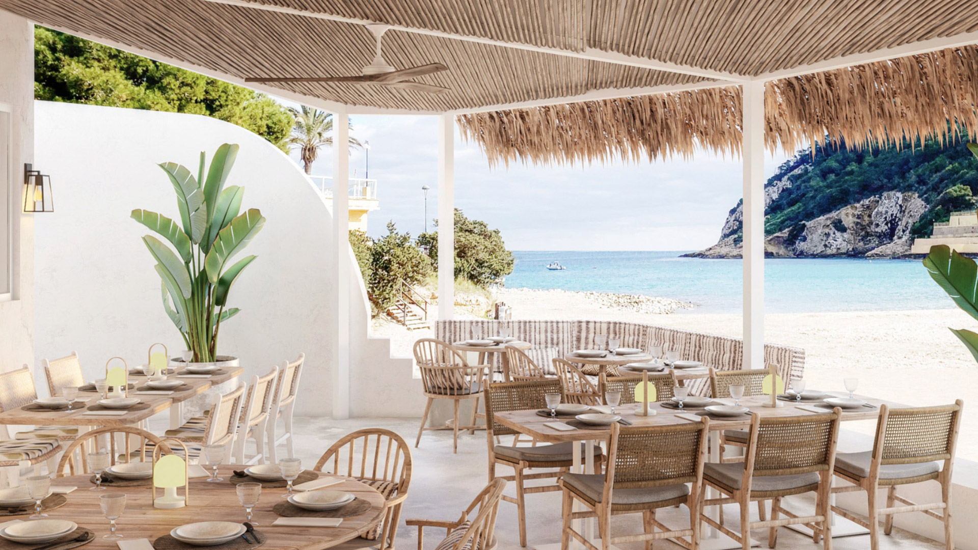 Outdoor restaurant with wicker chairs, light brown tables, white walls, green plants, and straw patio cover overlooking the beach and blue sea