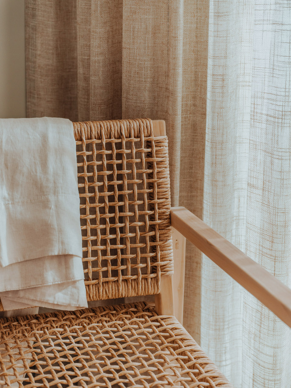 Close up of light brown wicker chair with beige linen throw blanket on the corner